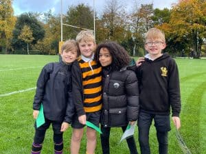 Group of diverse children standing on a rugby field at Inchmarlo, smiling and enjoying outdoor activity.