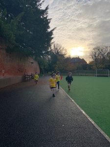 Children running on Inchmarlo community sports field at sunset.