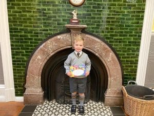 Young boy holding a gift box in front of a decorative fireplace in Inchmarlo setting.