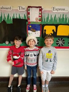 Three children smiling in festive sweaters at Inchmarlo nursery classroom.