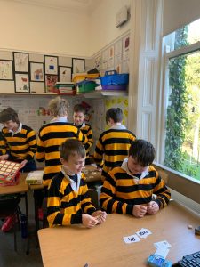 Students wearing yellow and black striped uniforms in classroom with bright window view.