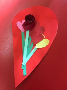 Colorful paper Valentine’s Day flower on a red heart background.