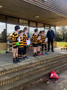 Children in school uniforms on a stage practicing music outdoors.