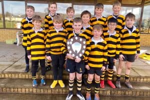 Young boys in black and yellow rugby uniforms outdoors with a trophy.