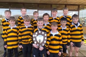 Group of young rugby players in striped jerseys holding a trophy.