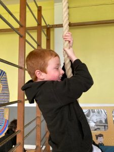 Child climbing rope at Inchmarlo activity center, outdoor play, kids fun in a vibrant setting.