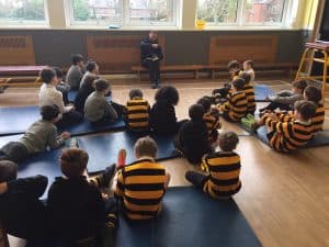 Students sitting on mats during an outdoor class session, engaged and listening attentively.