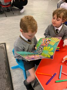 Two young students reading colorful picture books at school table, engaging in early childhood education.