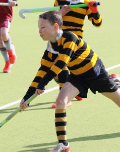 Young boy playing field hockey outdoors at Inchmarlo School.