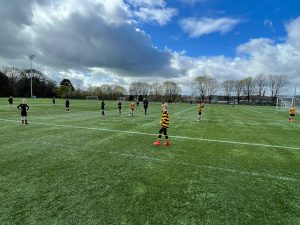 Children playing soccer on Inchmarlo sports field under a partly cloudy sky.