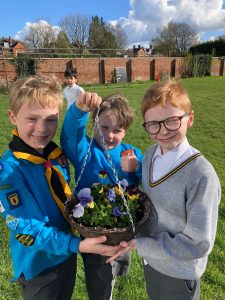 Three children holding an Easter basket with flowers outdoors.