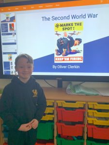 Young boy standing in classroom with educational display about WWII.