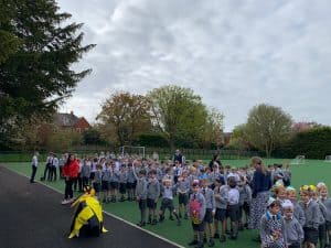 Large group of children and teachers gathered outdoors for a school event on a sports field.
