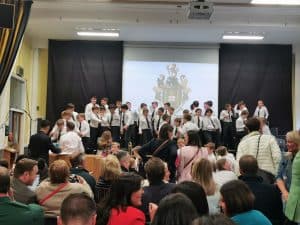 Students performing on stage at Inchmarlo School event, with an audience in the background.