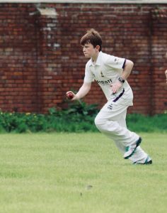 Young boy playing cricket outdoors on lush green field.