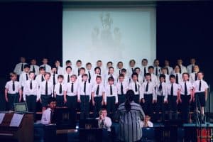 A large group of children singing on stage at Inchmarlo, showcasing musical talent in a vibrant setting.