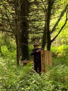 Person installing birdhouse in lush forest at Inchmarlo Resort, scenic outdoor nature setting.