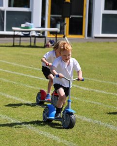 Children riding scooters on lush green outdoor sports field.