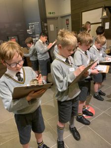Children reading books in school hall, engaging in educational activities.