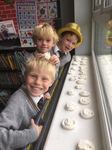 Three children smiling at Inchmarlo Preschool, engaging in a fun activity with clay models.