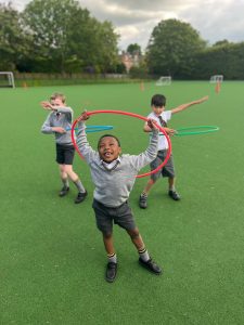 Three children playing with hula hoops on the Inchmarlo school field.