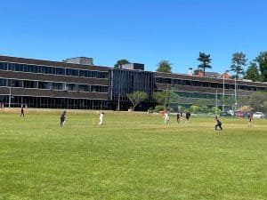 Modern school building with large playing fields and students playing sports outside.