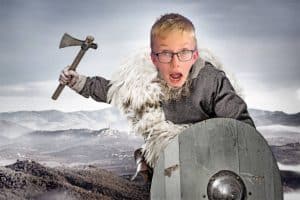 Child dressed as a Viking warrior with axe and shield outdoors.