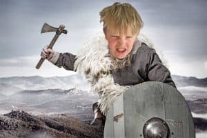 A young boy dressed as a Viking with an axe and shield in a rugged landscape.