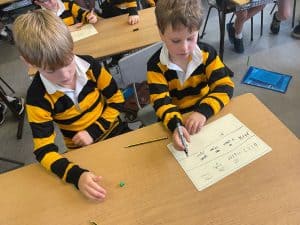 Two young boys working on a math worksheet in a classroom.