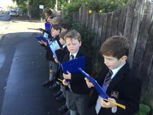 Children holding clipboards outdoors at Inchmarlo School in a neat row.