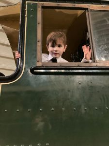Adorable young boy waving from vintage train carriage at Inchmarlo. Perfect for heritage travel and family fun.