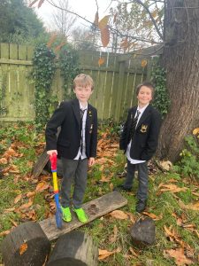 Two children in school uniforms outdoors at Inchmarlo, surrounded by autumn leaves and trees.