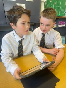 Two young boys in school uniforms using a tablet in classroom.