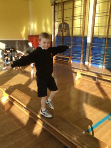 Child playing in school gymnasium with wooden benches and gym equipment.