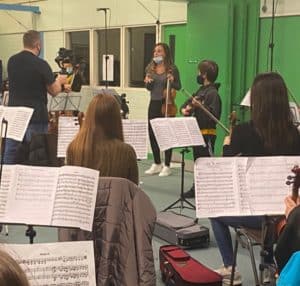Young musicians rehearse with a conductor in a studio setting.
