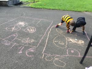 Two children drawing hopscotch game on asphalt with chalk in an outdoor school setting.