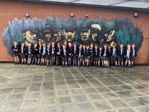 Group of school children standing outdoors in front of a vibrant mural, representing community and education.