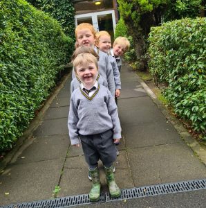 Children smiling outside Inchmarlo nursery, outdoors, greenery, joyful learning environment.
