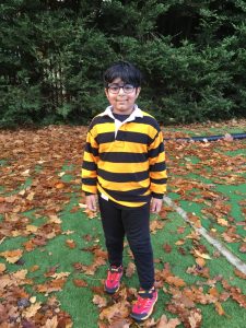 Young boy standing outdoors at Inchmarlo with fallen leaves and lush greenery in background.