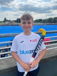 Young boy holding hockey stick at outdoor sports field, sunny day, sports and outdoor activity.