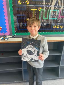 Young boy holding space-themed artwork at Inchmarlo School in Aberdeenshire, engaging in creative learning.